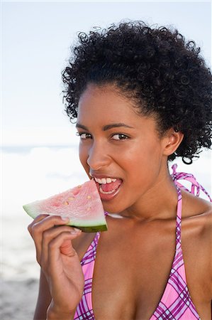 Young attractive woman sitting on the beach while eating a piece of watermelon Stock Photo - Premium Royalty-Free, Code: 6109-06004167
