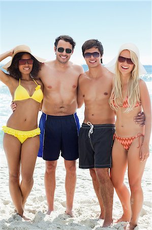Deux hommes et deux femmes en maillots de bain smaile comme ils mettent leurs bras autour de l'autre sur la plage Photographie de stock - Premium Libres de Droits, Code: 6109-06004195