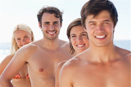 Two men and two women standing near each other while smiling by the sea with focus on the man at the back Stock Photo - Premium Royalty-Free, Code: 6109-06004251