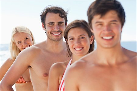 Two men and two women wearing swimsuits standing in single file by the sea with focus on the last three people Stock Photo - Premium Royalty-Free, Code: 6109-06004252