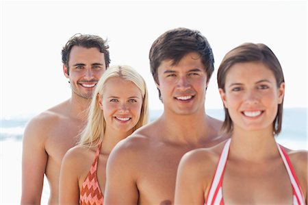 Two men and two women in swimsuits smiling as they stand behind each other with focus on the last two people Stock Photo - Premium Royalty-Free, Code: 6109-06004255