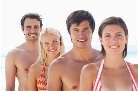 Two women and two men in swimsuits smiling as they stand behind each other on a beach with focus on the last two people Stock Photo - Premium Royalty-Free, Code: 6109-06004256