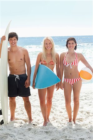 Man and two women standing on the beach in swimsuits as they are holding surfboards and a beach ball Stock Photo - Premium Royalty-Free, Code: 6109-06004201