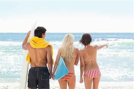 simsearch:6109-06004181,k - Two women and a man in swimsuits looking at the sea and pointing as the stand on a beach Foto de stock - Royalty Free Premium, Número: 6109-06004202