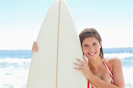 simsearch:6109-06004206,k - Woman in bikini smiling as she holds a surfboard closely with two hands on the beach Foto de stock - Sin royalties Premium, Código: 6109-06004209