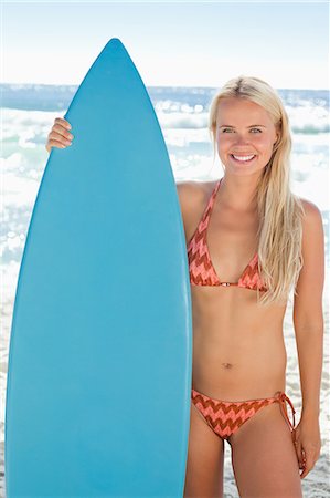 pretty women in bathing suits - Woman smiling while she holds her arm around a surfboard on the beach Stock Photo - Premium Royalty-Free, Code: 6109-06004217