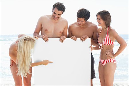 people holding a poster - Woman in a bikini pointing at a large blank poster while holding it with her three friends Stock Photo - Premium Royalty-Free, Code: 6109-06004233