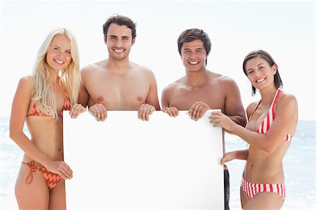 simsearch:6109-06004181,k - Two men and two women smiling as they hold a blank poster between them by the sea Foto de stock - Royalty Free Premium, Número: 6109-06004235