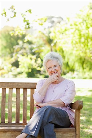 Woman smiling happily as she rests he head on her hand while sitting on a bench in the park Stock Photo - Premium Royalty-Free, Code: 6109-06004659