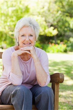 Woman smiling happily as she holds her head with her two hands while she sits on a bench Stock Photo - Premium Royalty-Free, Code: 6109-06004663