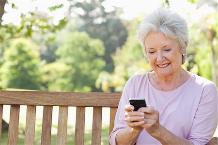 Woman smiling while using her phone as she sits on a bench in the park Stock Photo - Premium Royalty-Free, Code: 6109-06004690