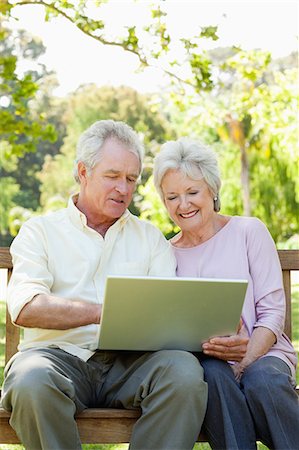 Man and a woman using a laptop while sitting together on a bench in a park Stock Photo - Premium Royalty-Free, Code: 6109-06004629