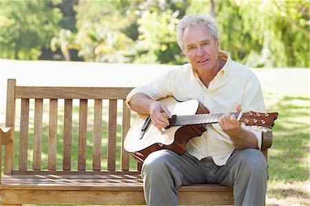 Homme regardant devant lui, alors qu'il joue une chanson sur une guitare, assis sur un banc dans le parc Photographie de stock - Premium Libres de Droits, Code: 6109-06004751