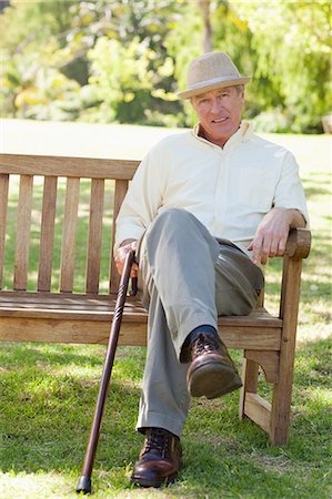 Homme portant chapeau en souriant alors qu'il est assis sur un banc et détient sa canne Photographie de stock - Premium Libres de Droits, Code: 6109-06004705