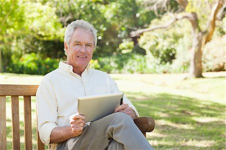 Man smiling while holding a tablet in the park Stock Photo - Premium Royalty-Free, Code: 6109-06004731
