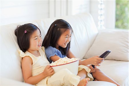 A side view shot of two sisters laughing together while watching tv and eating popcorn Stock Photo - Premium Royalty-Free, Code: 6109-06004847