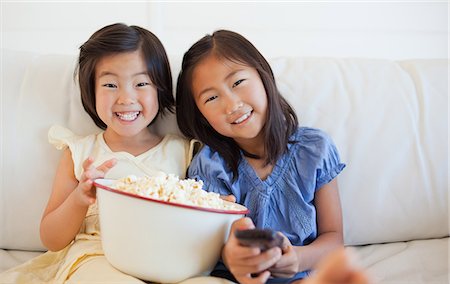 smiling kid eating bowl - Two sisters enjoying popcorn and television while laughing together. Stock Photo - Premium Royalty-Free, Code: 6109-06004846