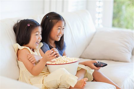 smiling laughing beauty - Side view of two sisters watching tv and eating popcorn while sitting on the couch Stock Photo - Premium Royalty-Free, Code: 6109-06004848