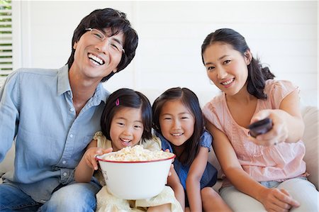 family watching tv together with popcorn - Family laughing and enjoying a funny show while sitting on the couch Stock Photo - Premium Royalty-Free, Code: 6109-06004858