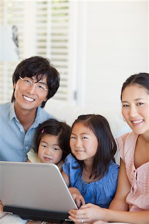 simsearch:6109-06004883,k - Happy family using the laptop together and looking forward while all sitting on the couch Foto de stock - Sin royalties Premium, Código: 6109-06004866