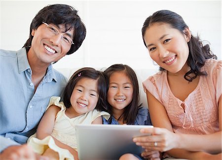 family tablet pc - Une famille heureuse, à l'aide d'un tablet pc et de regarder droit devant en souriant Photographie de stock - Premium Libres de Droits, Code: 6109-06004868