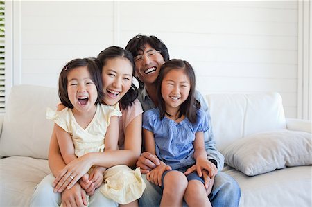 simsearch:6109-06004883,k - A family smiling and laughing as they sit together on the couch Foto de stock - Sin royalties Premium, Código: 6109-06004880