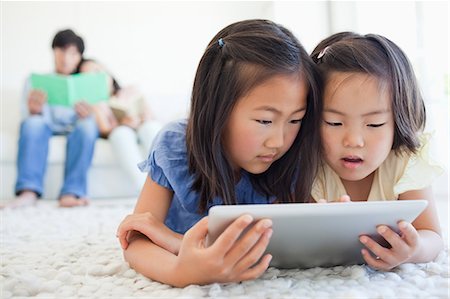The kids lie on the floor while reading a tablet pc as the parents read a book together Stock Photo - Premium Royalty-Free, Code: 6109-06004890