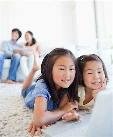 The parents sit and look to the side while the girls on the floor watch the laptop Stock Photo - Premium Royalty-Free, Code: 6109-06004897