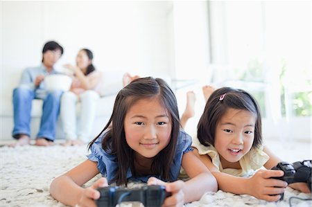 Kids look forward as they play a game while the parents eat and talk while they sit on the couch Stock Photo - Premium Royalty-Free, Code: 6109-06004895