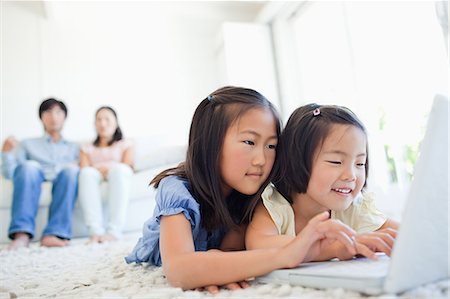 smiling brunette man looking at laptop - The parents sit on the couch while watching the children as they use the laptop Stock Photo - Premium Royalty-Free, Code: 6109-06004896