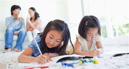 The girls on the floor draw and colour as the parents on the couch sit and chat Foto de stock - Sin royalties Premium, Código: 6109-06004898