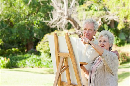 Man and a woman smiling while painting on a canvas in a park Stock Photo - Premium Royalty-Free, Code: 6109-06004815