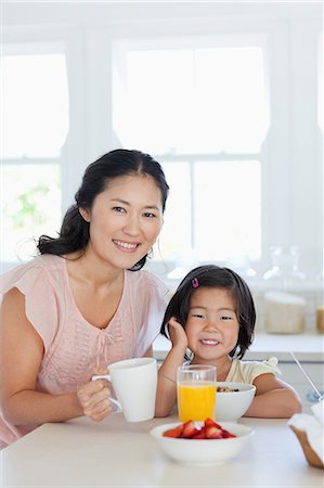 Une fille et sa mère assis ensemble et souriant à la table où ils sont sur le point de manger certains aliments Photographie de stock - Premium Libres de Droits, Code: 6109-06004995