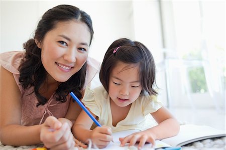 A mother looks up and smiles while her daughter continues to colour Stock Photo - Premium Royalty-Free, Code: 6109-06004904