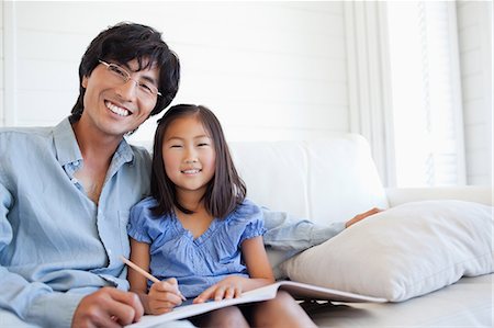 A smiling daughter and her dad sit at the couch while working on her homework Foto de stock - Sin royalties Premium, Código: 6109-06004912