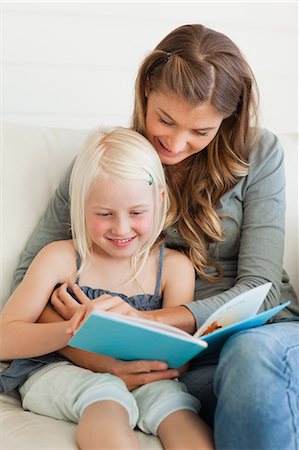 A mother and daughter sit together on the couch while reading a book and smiling Stock Photo - Premium Royalty-Free, Code: 6109-06005041