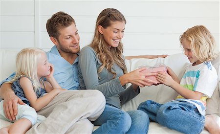 dar - The happy family sit on the couch smiling together as the mother hands her son a present Foto de stock - Sin royalties Premium, Código: 6109-06005058