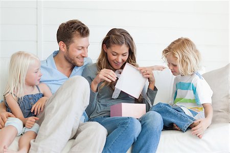 dad gifted kid - The family sit happily on the couch as they all watch the mother open her present with joy Stock Photo - Premium Royalty-Free, Code: 6109-06005061