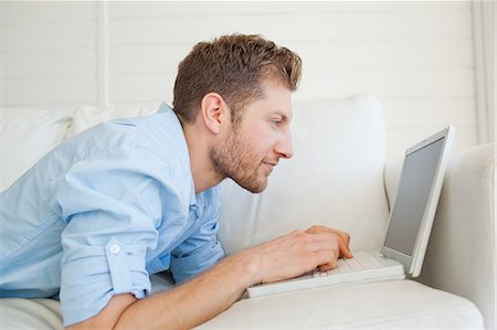 dactylographier - Un homme à l'aide de son ordinateur portable, car il se trouve dans son canapé Photographie de stock - Premium Libres de Droits, Code: 6109-06005075