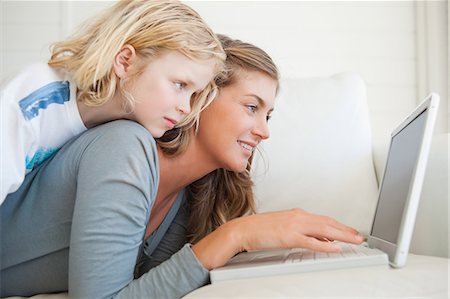 A child lies up on top of her mother as she uses the laptop on the couch and smiles Stock Photo - Premium Royalty-Free, Code: 6109-06005092