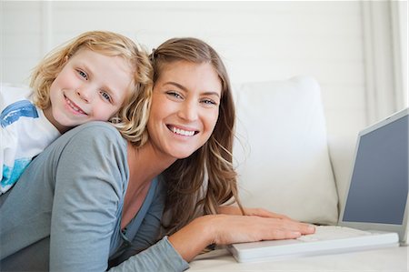 A smiling mother and son lie on the couch and uses the laptop as they look forward Stock Photo - Premium Royalty-Free, Code: 6109-06005096