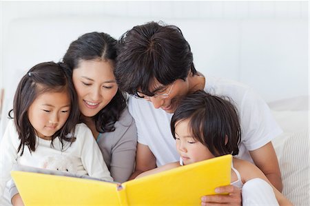A close up shot of the family sitting on the bed and reading a story book Stock Photo - Premium Royalty-Free, Code: 6109-06005013