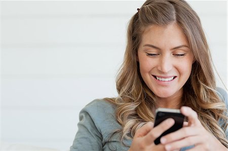 A smiling woman who is sitting while she uses her phone to send a text message Stock Photo - Premium Royalty-Free, Code: 6109-06005031