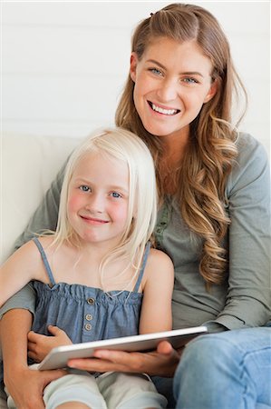 The girl and woman look straight ahead as they sit on the couch with a tablet pc in front of the girl Stock Photo - Premium Royalty-Free, Code: 6109-06005038