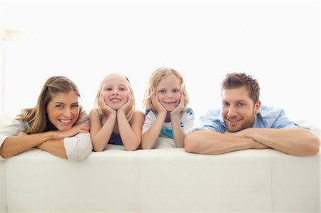 simsearch:6109-06005142,k - A smiling family with the parents arms folded and the kids hands holding their heads up while they sit on the back of the couch Stock Photo - Premium Royalty-Free, Code: 6109-06005140