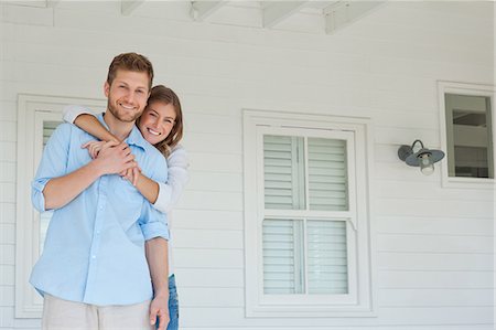 A smiling wife holding onto her husband as they stand on the porch while looking forward Foto de stock - Sin royalties Premium, Código: 6109-06005187