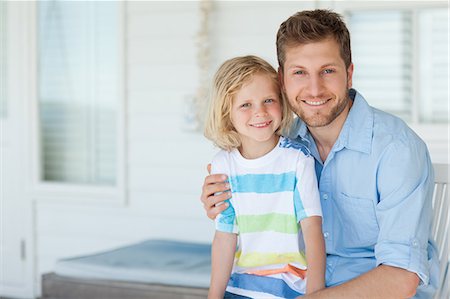 A smiling dad and his son sit on the seat together just outside of the house Stock Photo - Premium Royalty-Free, Code: 6109-06005215