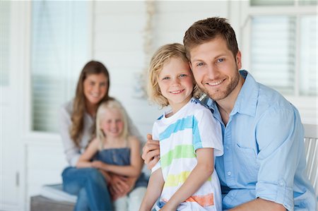 A smiling family sit with the father and son in the front and the daughter and wife in the background Stock Photo - Premium Royalty-Free, Code: 6109-06005216