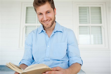 A man looks up from the book for a moment while he smiles Stock Photo - Premium Royalty-Free, Code: 6109-06005222