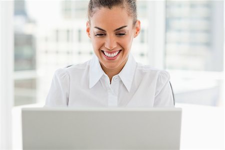 Frizzy haired smiling woman working with a laptop in a bright office Stock Photo - Premium Royalty-Free, Code: 6109-06005353